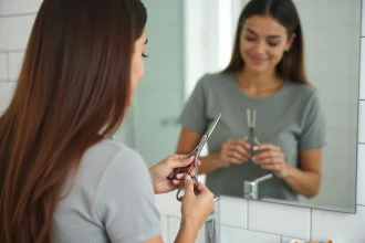Femme qui se coupe les pointes elle-même devant un miroir de salle de bain avec des ciseaux professionnels