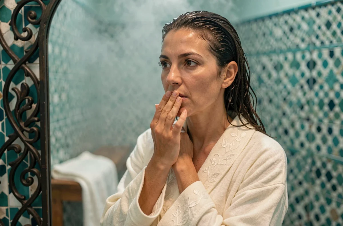 Femme marocaine vérifiant son maquillage à l'aker fassi devant un miroir dans un hammam traditionnel