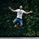 man wearing t-shirt and jeans jumpshot in front of a green hedge