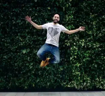 man wearing t-shirt and jeans jumpshot in front of a green hedge